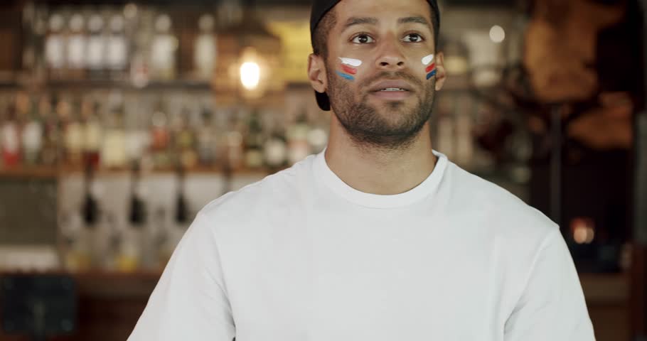 Male football fan with painted face watching match at pub and he is upset about team loss. Portrait of worried hispanic man cheering at soccer game and feeling frustration