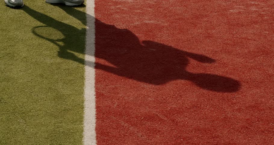 Shadow of woman playing tennis and serving ball with racket at clay court. Woman play sports at sunny summer day and training to hitting ball. Active leisure concept. Player preparing to competition
