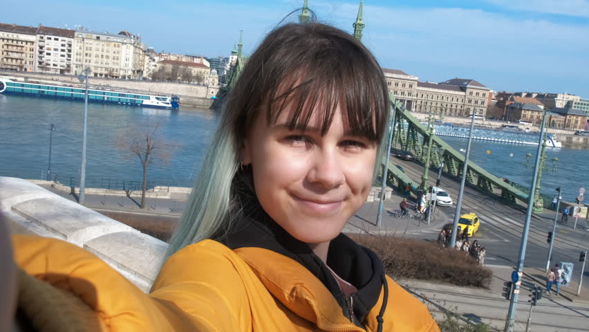 Taking photo by danube river. A modern young girl takes photo and video from the city outdoor balcony against Budapest landmark.