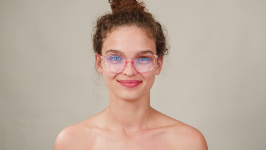 Young attractive brunette woman with curly hair in a bun wearing pink glasess close-up, white background. Portrait