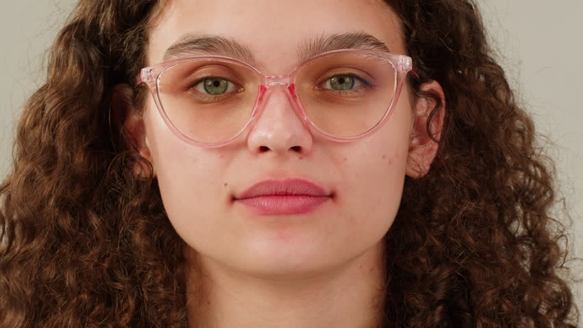 Young attractive brunette woman with curly hair in a bun wearing pink glasess close-up, white background. Portrait