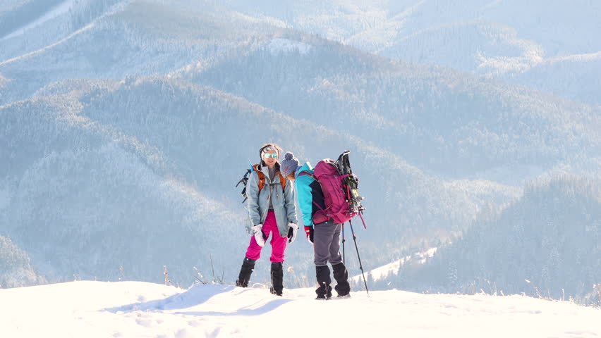 two women on top of the mountain. during a winter hike, winter hike, two girlfriends traveling together, snowy mountains, girl high-fiving her friend