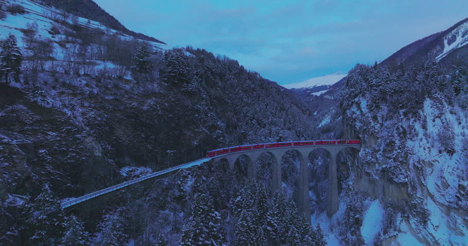 Landwasser Viaduct world heritage sightseeing Glacier and Bernina express in Swiss Alps snow winter scenery at night. Aerial Drone shot red train passing through famous mountain. Filisur, Switzerland. | Shutterstock HD Video #1110899727