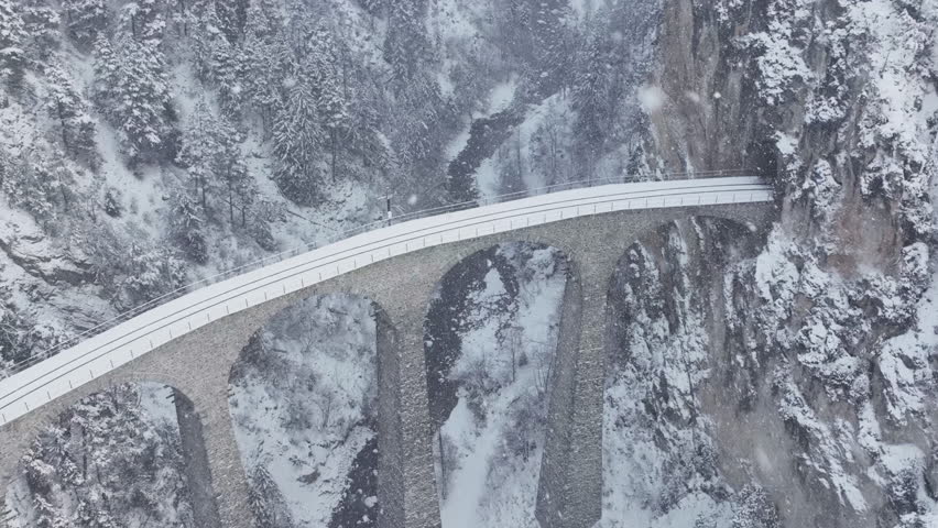 Aerial drone view Landwasser Viaduct world heritage sightseeing with luxury Glacier express train in Swiss Alps snow winter day scenery. Panoramic railway scenic in Switzerland. Snowing, Slow motion. | Shutterstock HD Video #1110899733
