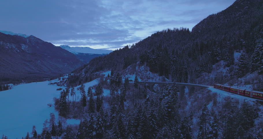 Landwasser Viaduct world heritage sightseeing Glacier and Bernina express in Swiss Alps snow winter scenery at night. Aerial Drone shot red train passing through famous mountain. Filisur, Switzerland. | Shutterstock HD Video #1110899735
