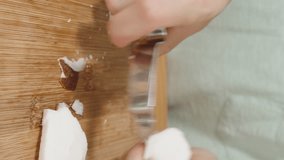 Vertical video. A Woman Takes Coconut Pieces from the Plate and Peels the Skin Off Them with a Specialized Knife. The Slider Captures It in Close-Up.