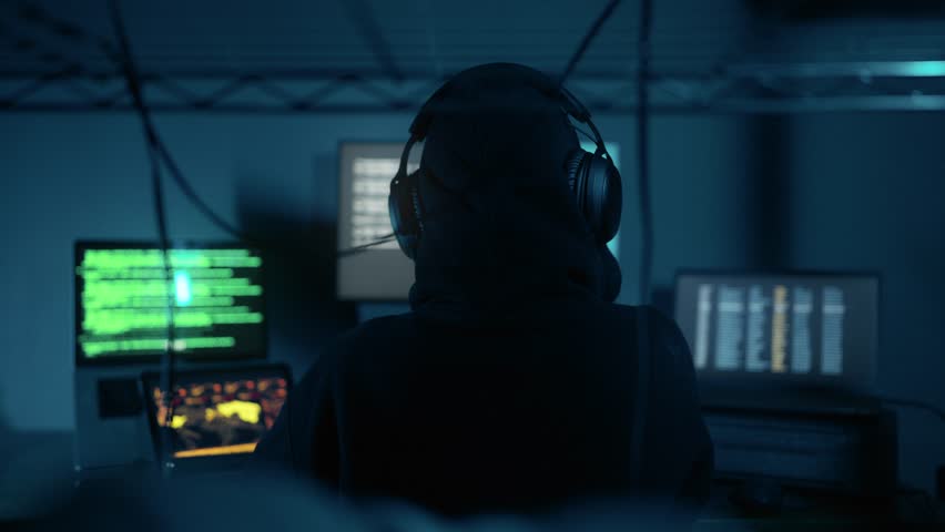 A hacker breaks into company data servers in dark atmosphere and has multiple displays. Hacker in dark room surrounded computers. Hacker breaks into corporate data server. Digital system security Royalty-Free Stock Footage #1110906963