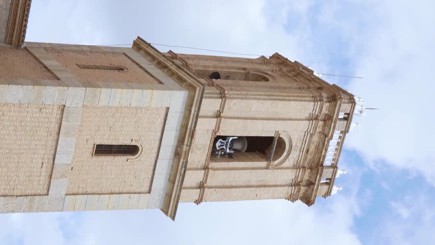 Close-up of a church bell tower with its bells ringing against a blue sky with clouds. Vertical video. Religious call concept