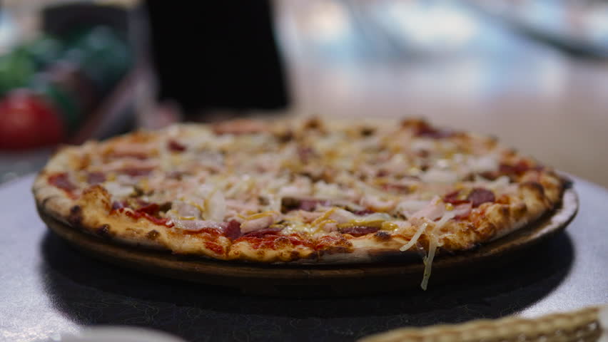 Large pizza stands on table in bowling alley near ball receptacle during game at party, static shot. Snack for group of friends and entertainment provided by pizzeria during ball toss indoor.