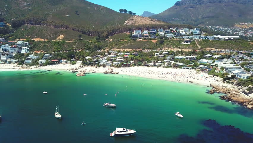 Beach, sea and boat with drone of mountains, city and holiday houses for travel, hospitality and vacation. Aerial view of people swimming, kayaking and ocean or location in Cape Town, South Africa