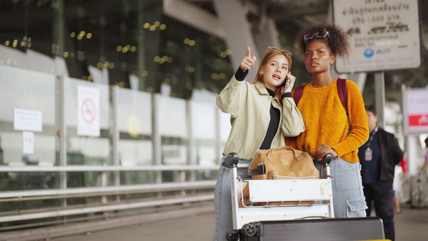 Happy woman friends with luggage trolley waiting for taxi go to hotel in the city together at airport terminal. Attractive girl enjoy travel on holiday vacation with airplane and public transportation | Shutterstock HD Video #1110920301