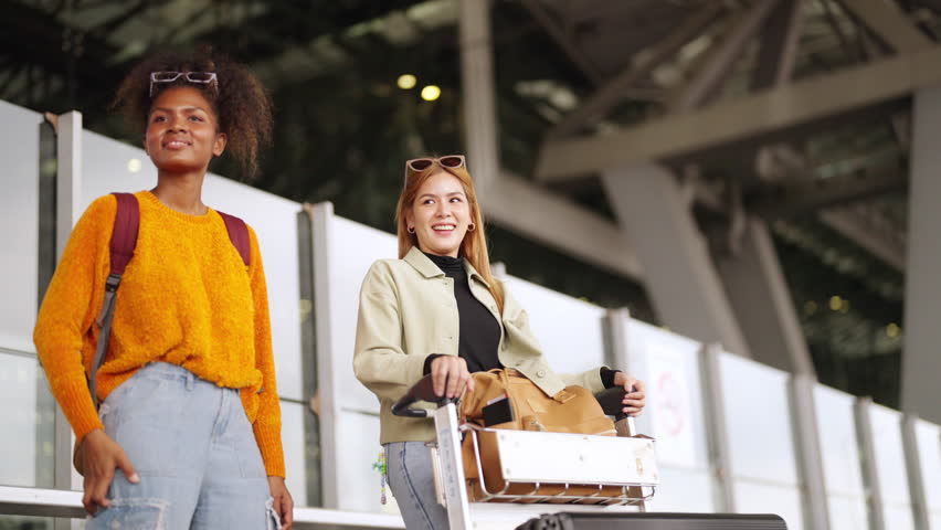 Happy woman friends with luggage trolley waiting for taxi go to hotel in the city together at airport terminal. Attractive girl enjoy travel on holiday vacation with airplane and public transportation | Shutterstock HD Video #1110920303