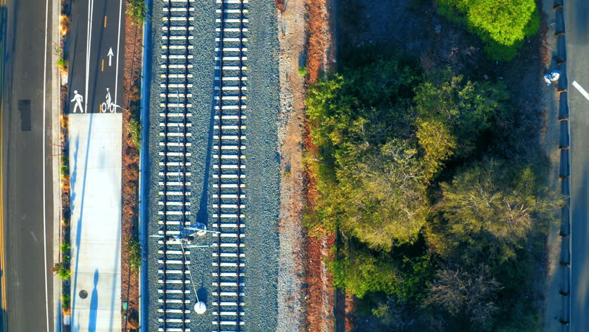 Aerial: Drone Top Backward Shot Of Railroad Tracks By Person Walking On Street In City - Culver City, California