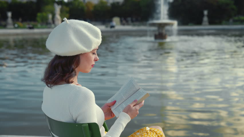 Attractive girl reading a book near a fountain in a park, Paris | Shutterstock HD Video #1110925917
