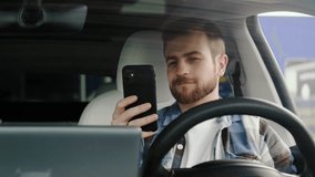 Smiling young man sitting in the car and looking at phone screen. Slow motion - Powered by Shutterstock - Get 15% off with code: PIKWIZARD15