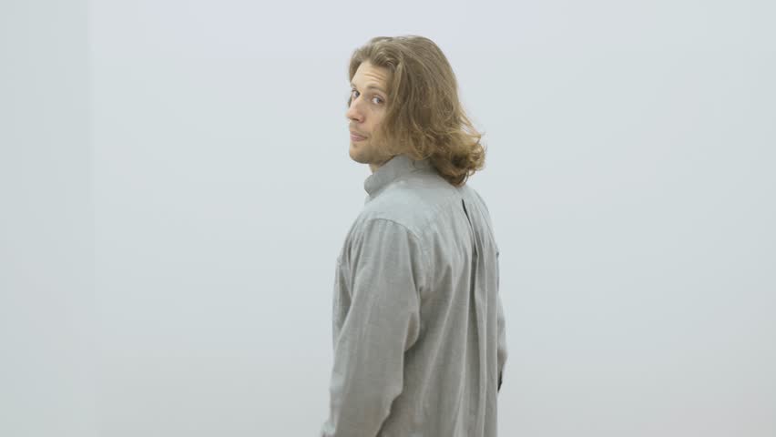 Young handsome caucasian man stands in front of a mirror and tries on gray shirt in a fitting room at the mall 4K