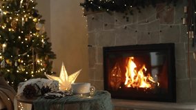 Merry Christmas! Stylish wrapped gift, gingerbread cookies and tea cup on table against festive christmas lights and burning fireplace. Cozy christmas eve. Winter hygge footage