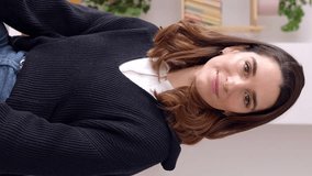 Portrait of young smiling businesswoman looking at camera standing at office workplace. Professional entrepreneur woman crossing her arms showing self-confidence. Vertical 9:16 HD screen footage.