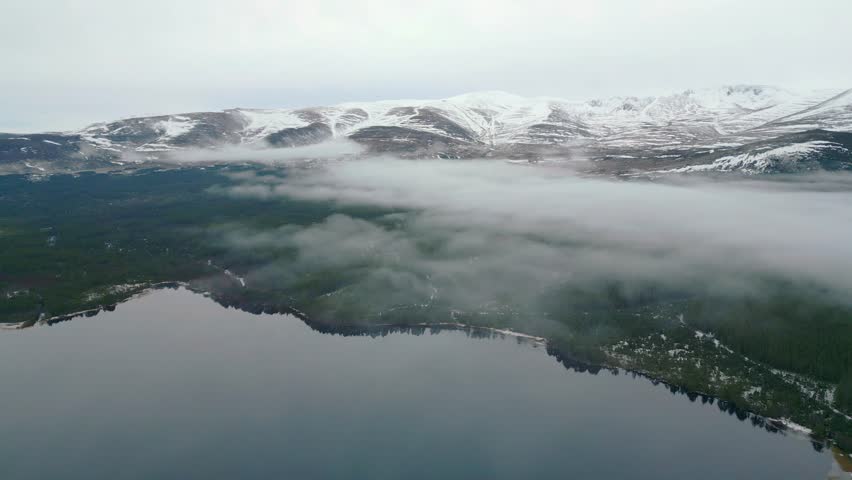 Flying through mist over a glass-like loch Ness towards snow-covered mountains 