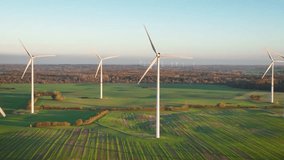 Aerial footage of wind turbines gracefully spin, one up close and lush forests landscapes provide the backdrop, with more wind turbines in the distance. Sustainable synergy of onshore and farming.