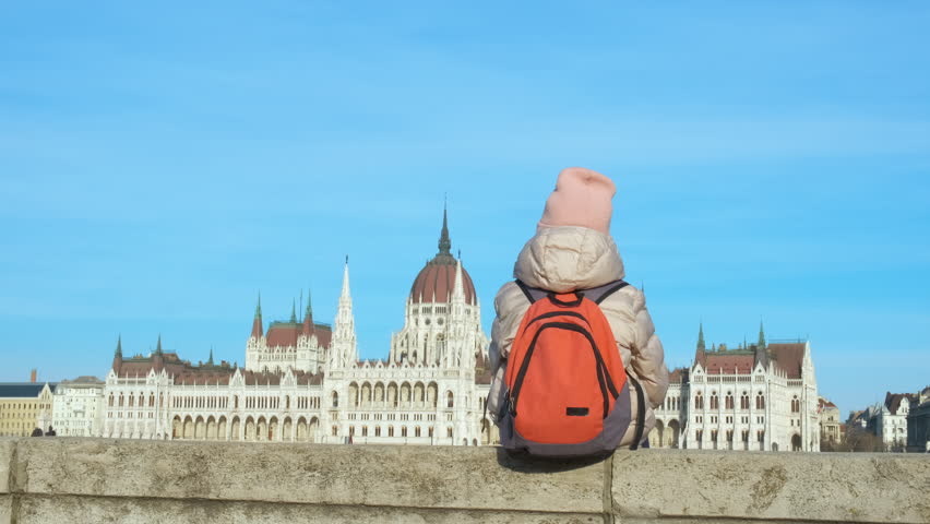 Little tourist at the parliament. A child sits with a backpack against the backdrop of the Budapest Parment in spring.