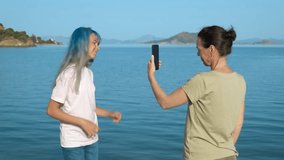 A mother is filming a video for her daughter. A teenage girl dances merrily on the beach, mom records a video on a smartphone.