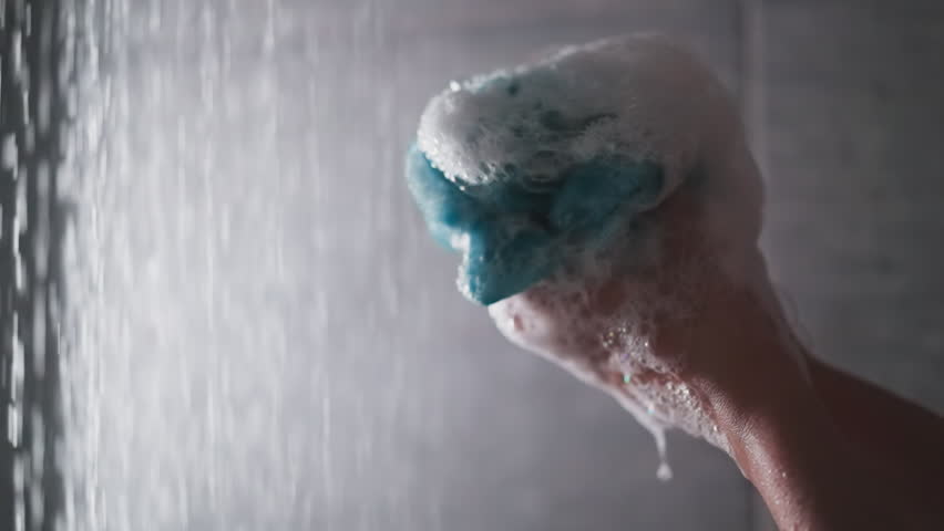 Woman squeezes loofah in shower cabin closeup. Lady hands hold foamy body washing sponge against water sprays. Soft supply for personal hygiene Royalty-Free Stock Footage #1110952769