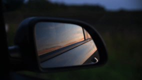 Close-up view of sunset sky reflecting in car's door mounted outer rear view mirror. Soft focus. Real time handheld video. Road trip theme.