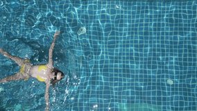Vertical video. Top view of young woman swimming on the back in the pool in slow motion.
