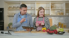 Positive attractive hearing impaired couple in aprons networking on digital tablet, choosing and discussing online recipe using sign language while preparing for cooking in domestic kitchen. - Powered by Shutterstock - Get 15% off with code: PIKWIZARD15
