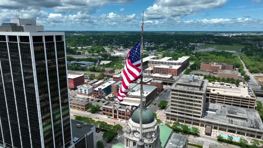 American flag waving above downtown Fort Wayne, Indiana. Aerial establishing shot of USA city with Allen County Courthouse in shot.