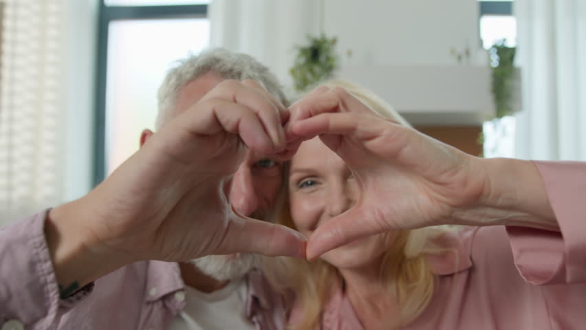 Close-up healthy elderly Caucasian family couple looking through joined fingers make heart shape symbol valentines day celebration romantic relationships eternal love happy long-life marriage concept
