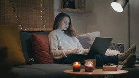 A young Caucasian woman working on a laptop while sitting on the sofa on a Christmas winter evening - Powered by Shutterstock - Get 15% off with code: PIKWIZARD15