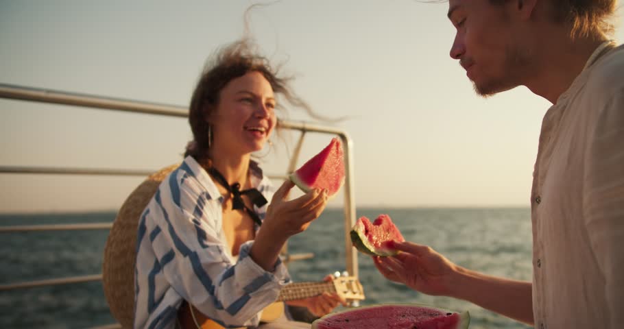 Happy couple guy and girl on a date and on the pier near the sea they eat watermelon and feed it to each other. Couple on a date near the sea on a picnic Royalty-Free Stock Footage #1110969943