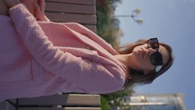 Beautiful Woman in a Pink Business Outfit Poses while sitting on a bench of a City Park on a Sunny Day. Fashion and Beauty Concept. Vertical Video, Slow Motion.
