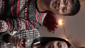Vertical Screen: smiling asian couple facing camera and raising their wineglasses to make a new yearâ€™s toast to friends while making video call in a festive living room at home