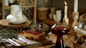 A horizontal 4K video featuring a slice of strawberry cake with cutlery, a cup of red steaming winter tea, and flickering candles, set on a wooden board for a cozy ambiance