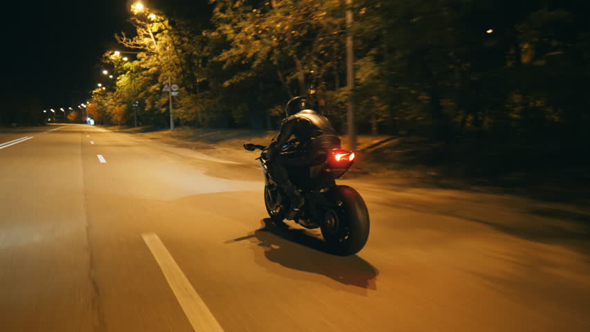Motorcyclist racing his motorcycle on evening city. Man riding on modern sport motorbike at night street of town. Guy driving bike during trip. Concept of freedom and adventure. Rear view Close up