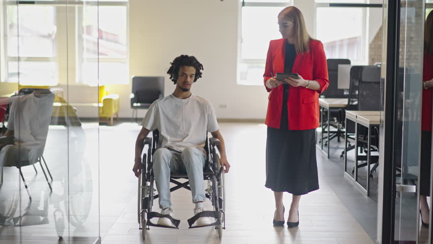 African American businessman in a wheelchair engages in a professional discussion with his colleague, addressing various business challenges and exploring solutions in an inclusive and diverse modern Royalty-Free Stock Footage #1110974079