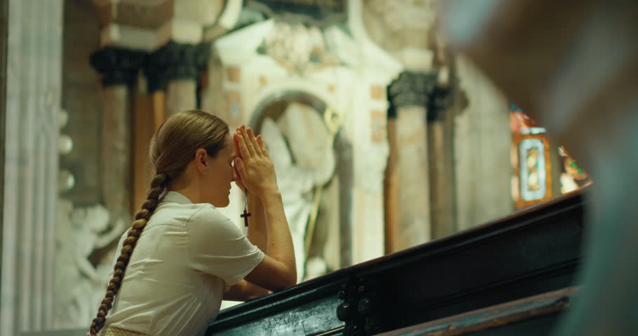 Adult girl knelt down in thanksgiving prayer to God in cathedral church. A sincerely believing woman face close-up.