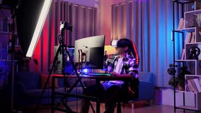 Asian Boy Streamer Playing Game Experience Virtual Reality In Futuristic Goggles. Player Touching Air Panel. Personal Computer On Desk Illuminated By Rgb Led Strip Light