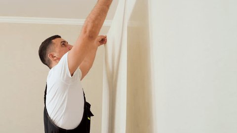 Professional Caucasian worker glues a strip of wallpaper on the wall. Man with dark hair in a uniform glueing wallpaper. స్టాక్ వీడియో