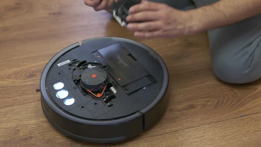 Caucasian young man doing vacuum cleaner robot maintenance. Male starts automatic vacuum cleaner. Robot vacuum cleaner repair. High quality photo