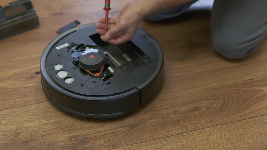 Caucasian young man doing vacuum cleaner robot maintenance. Male starts automatic vacuum cleaner. Robot vacuum cleaner repair. High quality photo