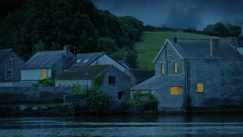 Houses By The River With Lights On At Dusk