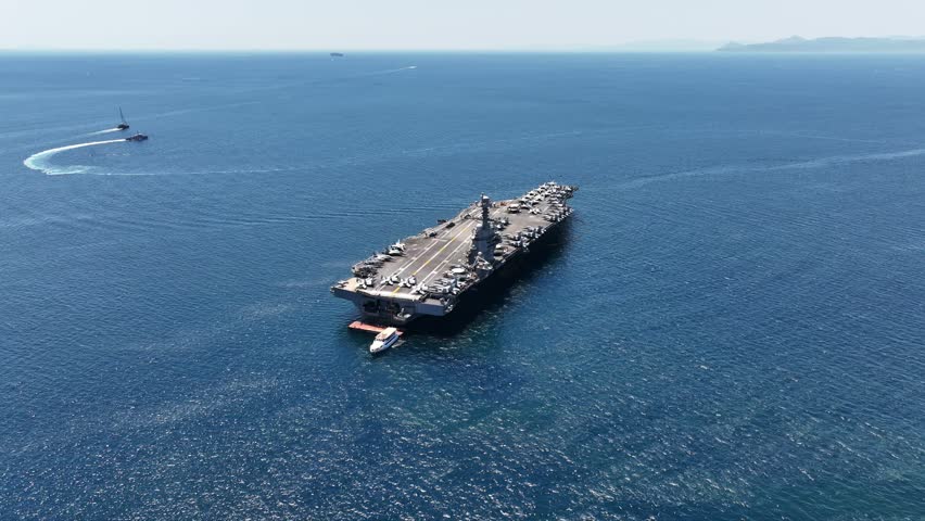 Aerial drone video of USS Gerald R. Ford latest technology nuclear powered aircraft carrier anchored in deep blue open ocean sea