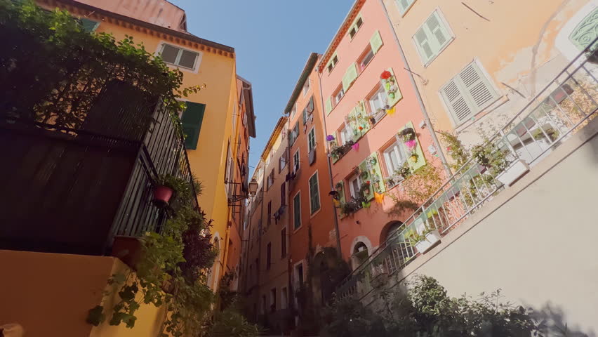 steps up among the narrow streets of the old city of Nice, France, laundry hanging drying on the facades of buildings, parked bicycles and bikes, lots of flowers on the windows, lanterns on the walls