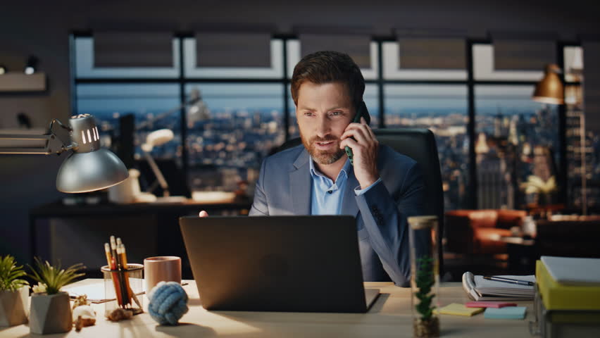 Smiling entrepreneur talking cellphone at night interior closeup. Confident executive discussing corporate strategy with partner on mobile phone call. Successful man consulting client. Evening office 