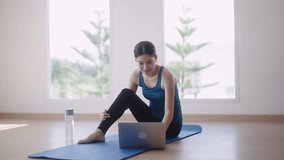 Asian female fitness trainer in workout is conducting online fitness classes through video call on her laptop to help students maintain their strength and good health while exercising at home