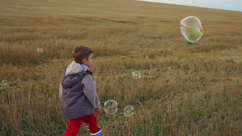 Boy having fun playing in a field with soap bubbles.